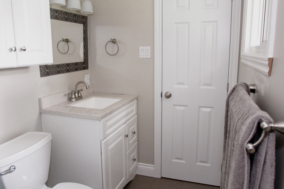 This is an example of a small traditional master bathroom in Ottawa with raised-panel cabinets, white cabinets, a shower/bathtub combo, a two-piece toilet, gray tile, grey walls, ceramic floors, an undermount sink and engineered quartz benchtops.