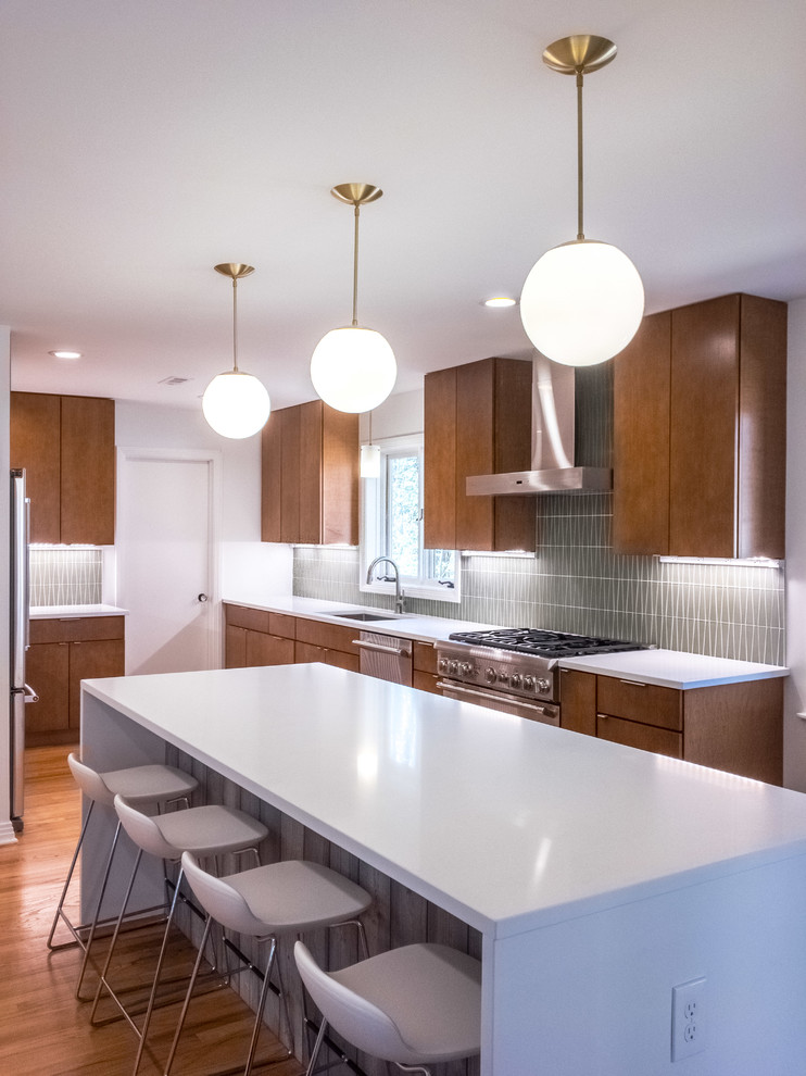 Design ideas for a large midcentury l-shaped open plan kitchen in Raleigh with an undermount sink, flat-panel cabinets, medium wood cabinets, quartz benchtops, green splashback, glass tile splashback, stainless steel appliances, medium hardwood floors and with island.