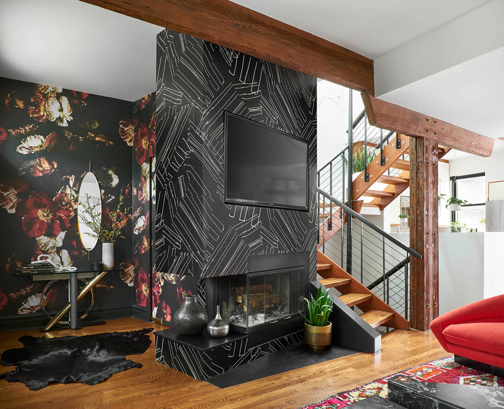 This is an example of a mid-sized eclectic open concept living room in Chicago with black walls, medium hardwood floors, a wall-mounted tv, a standard fireplace and brown floor.