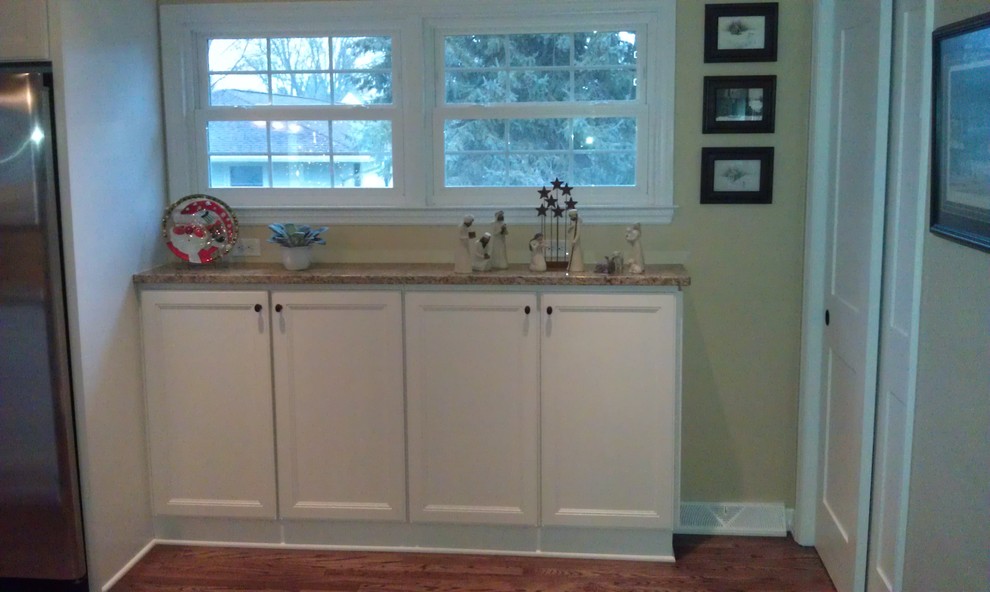 Mid-sized transitional l-shaped eat-in kitchen in Milwaukee with a farmhouse sink, flat-panel cabinets, yellow cabinets, granite benchtops, stainless steel appliances, light hardwood floors, a peninsula, beige splashback and stone slab splashback.