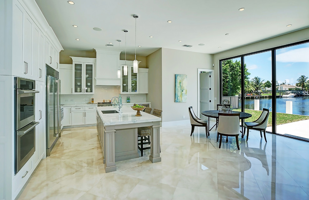 Photo of a mid-sized tropical l-shaped eat-in kitchen in Miami with an undermount sink, recessed-panel cabinets, white cabinets, quartz benchtops, white splashback, porcelain splashback, stainless steel appliances, marble floors, with island and beige floor.