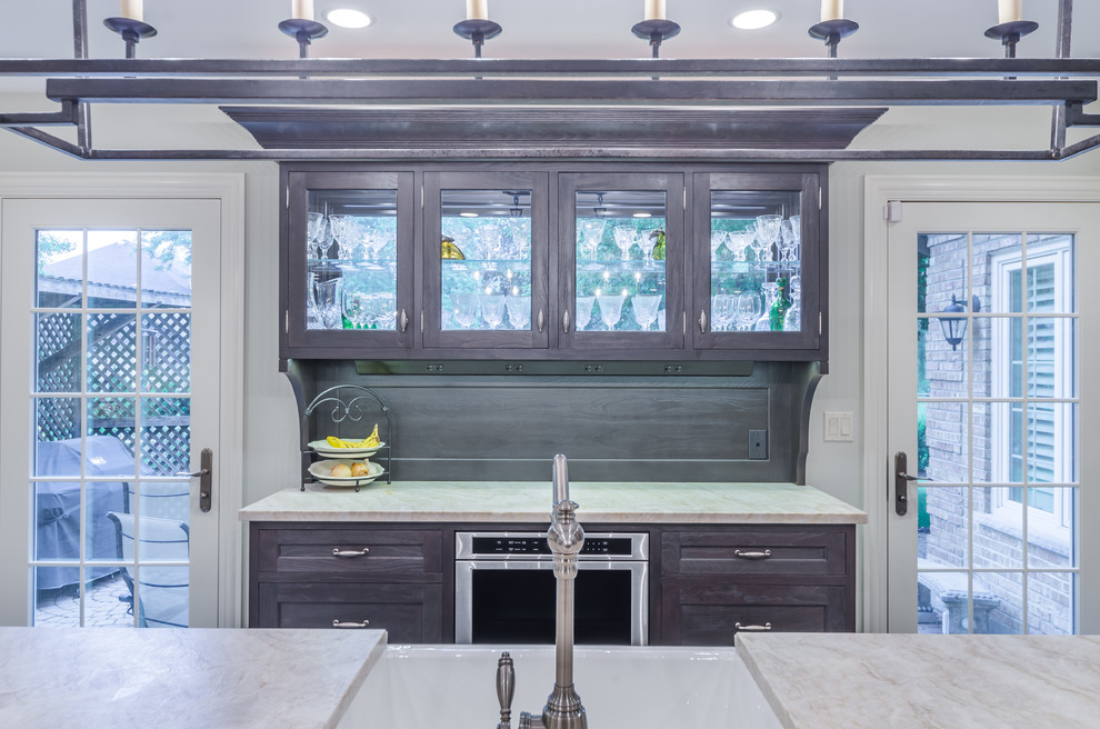 Inspiration for a mid-sized traditional galley eat-in kitchen in Chicago with a farmhouse sink, marble benchtops, white splashback, ceramic splashback, stainless steel appliances, painted wood floors, with island, multi-coloured floor, glass-front cabinets, black cabinets, grey benchtop and exposed beam.