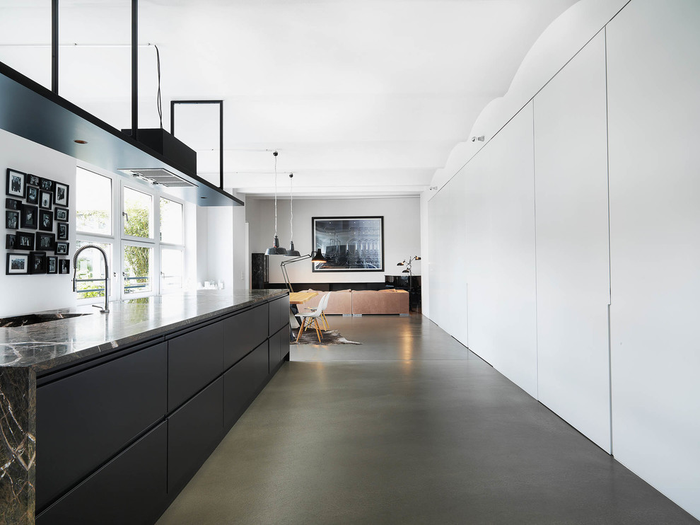Design ideas for an expansive contemporary open plan kitchen in Berlin with flat-panel cabinets, black cabinets, with island, an undermount sink, marble benchtops and concrete floors.