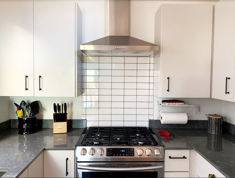 This is an example of a small midcentury u-shaped separate kitchen in Other with an undermount sink, flat-panel cabinets, white cabinets, quartz benchtops, grey splashback, stainless steel appliances, cork floors, beige floor and grey benchtop.