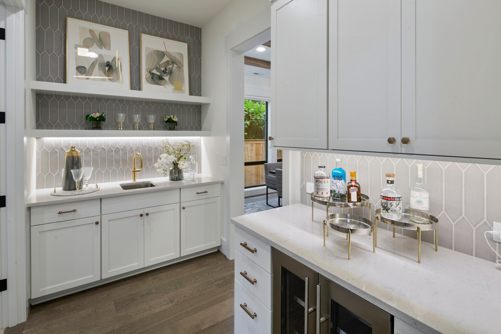 Design ideas for a mid-sized l-shaped wet bar in Seattle with an undermount sink, recessed-panel cabinets, white cabinets, quartz benchtops, grey splashback, cement tile splashback, light hardwood floors, brown floor and white benchtop.