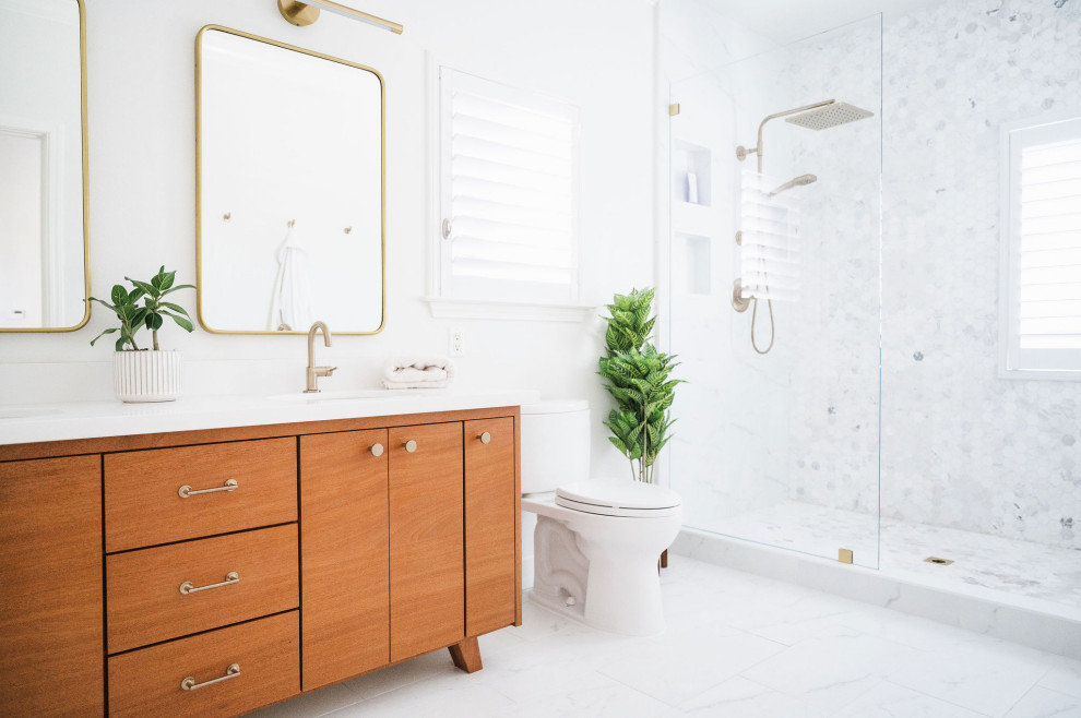 This is an example of a mid-sized beach style bathroom in San Francisco with flat-panel cabinets, medium wood cabinets, a curbless shower, a one-piece toilet, white tile, ceramic tile, white walls, porcelain floors, an integrated sink, quartzite benchtops, white floor, an open shower, white benchtops, a niche, a double vanity and a built-in vanity.