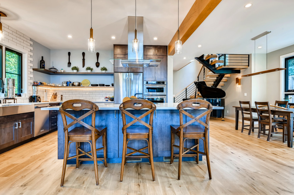 This is an example of a mid-sized contemporary l-shaped eat-in kitchen in Denver with a farmhouse sink, shaker cabinets, dark wood cabinets, quartzite benchtops, beige splashback, subway tile splashback, stainless steel appliances, light hardwood floors, with island, brown floor, beige benchtop and exposed beam.