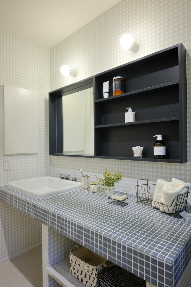 This is an example of a contemporary powder room in Sapporo with open cabinets, gray tile, white tile, grey walls, a drop-in sink, tile benchtops and beige floor.