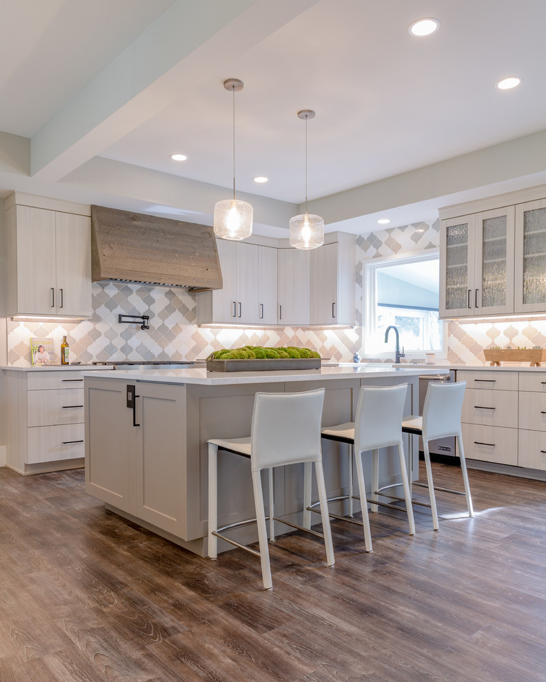 Large contemporary l-shaped open plan kitchen in Denver with a farmhouse sink, flat-panel cabinets, grey cabinets, quartz benchtops, grey splashback, porcelain splashback, stainless steel appliances, laminate floors, grey floor, white benchtop and with island.
