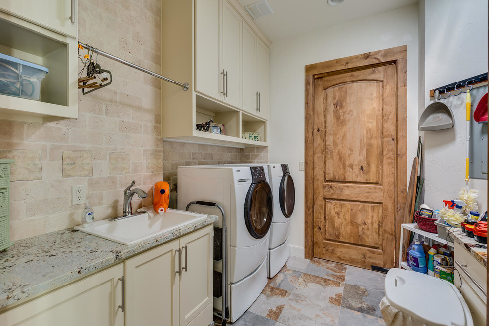 Design ideas for a mid-sized country single-wall dedicated laundry room in Austin with a drop-in sink, recessed-panel cabinets, white cabinets, granite benchtops, white walls, slate floors, a side-by-side washer and dryer and multi-coloured floor.
