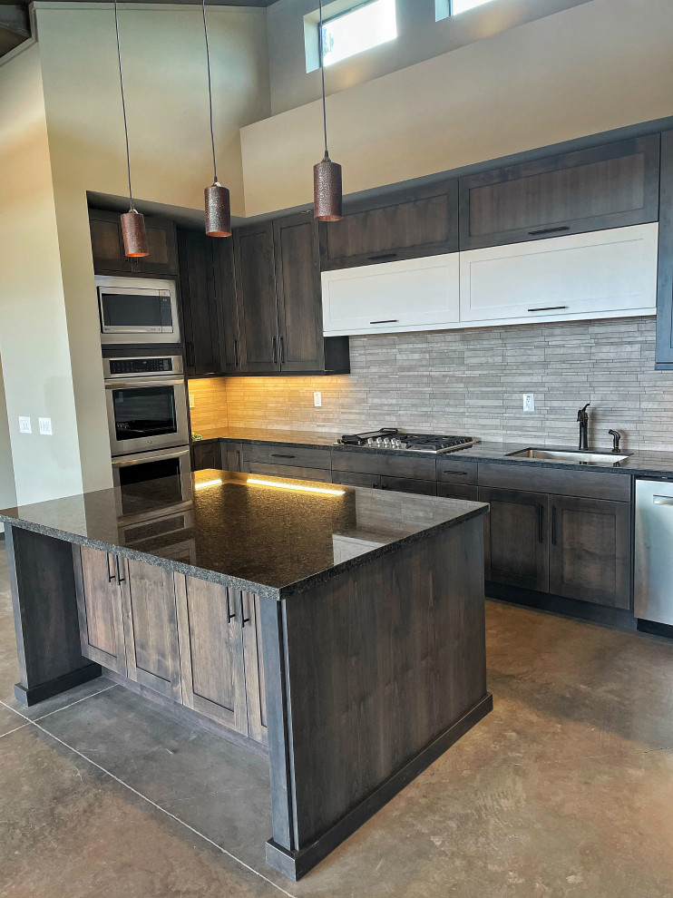 Inspiration for a mid-sized contemporary u-shaped separate kitchen in Phoenix with an undermount sink, shaker cabinets, distressed cabinets, granite benchtops, beige splashback, limestone splashback, stainless steel appliances, concrete floors, with island, grey floor and black benchtop.