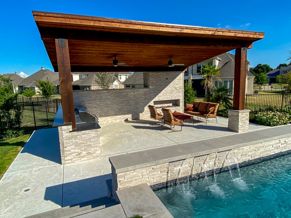 This is an example of a large modern backyard custom-shaped infinity pool in Dallas with a water feature and stamped concrete.