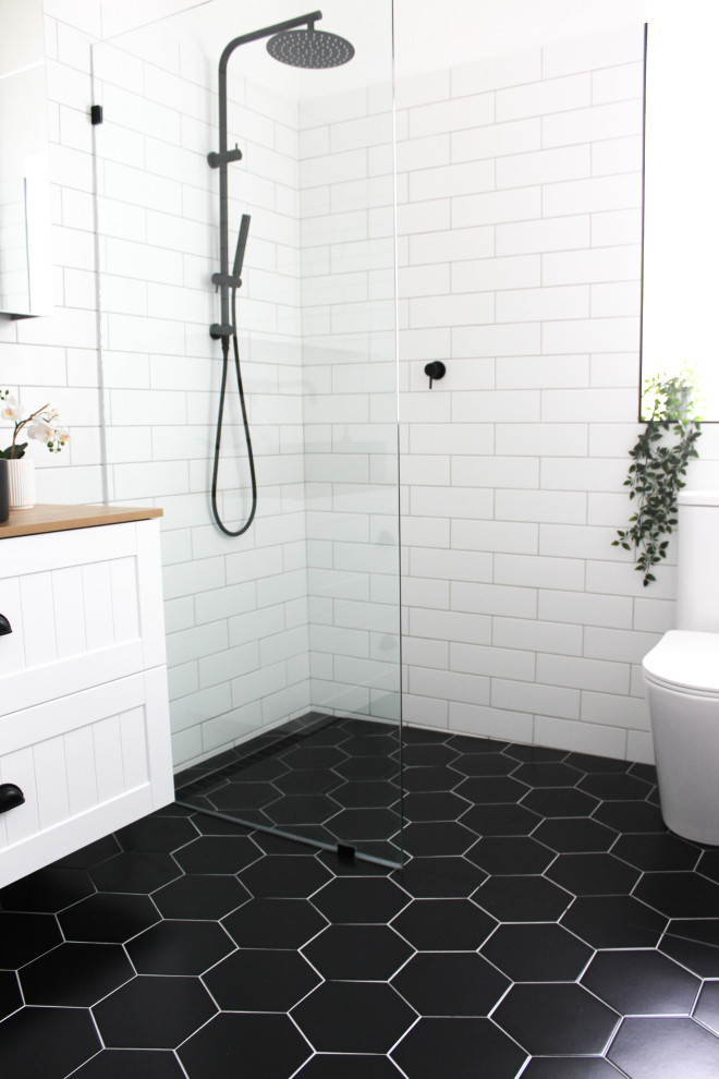 This is an example of a small modern kids bathroom in Perth with shaker cabinets, white cabinets, an open shower, a one-piece toilet, white tile, ceramic tile, white walls, porcelain floors, a vessel sink, wood benchtops, black floor, an open shower, beige benchtops, a single vanity, a floating vanity and brick walls.