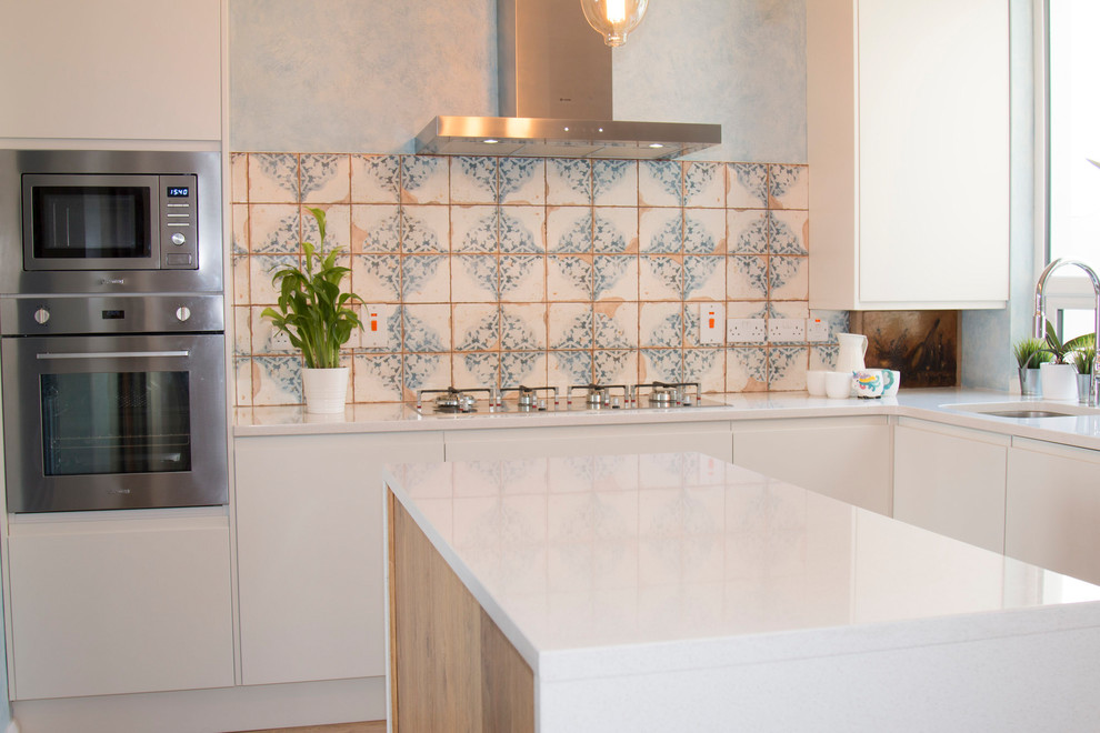 Inspiration for a small bohemian l-shaped open plan kitchen with a built-in sink, flat-panel cabinets, beige cabinets, quartz worktops, beige splashback, cement tile splashback, stainless steel appliances, laminate floors, an island and brown floors.