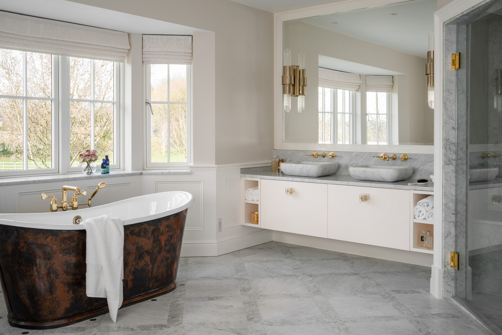 This is an example of a large transitional master bathroom in London with flat-panel cabinets, white cabinets, a freestanding tub, marble, marble floors, grey floor, a hinged shower door, gray tile, beige walls, a vessel sink and grey benchtops.