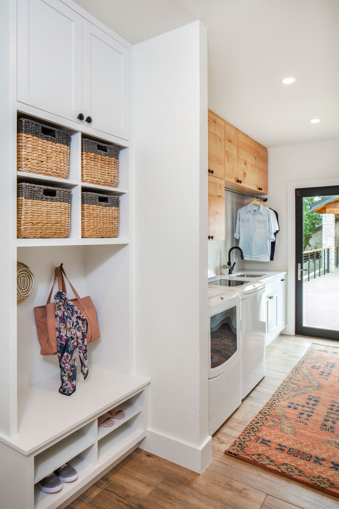 Inspiration for a country utility room in Austin with an undermount sink, white walls, a side-by-side washer and dryer, shaker cabinets, white cabinets, brown floor and white benchtop.
