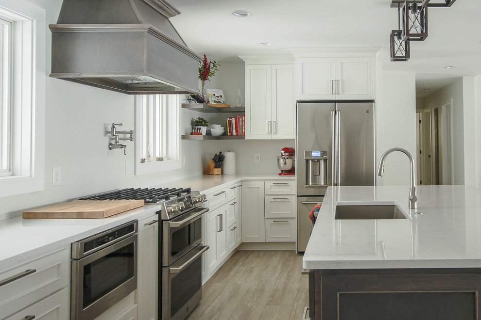 Photo of a large transitional l-shaped eat-in kitchen in Detroit with a triple-bowl sink, shaker cabinets, white cabinets, quartz benchtops, stainless steel appliances, medium hardwood floors, with island, brown floor and white benchtop.