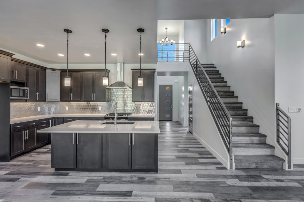 Mid-sized elegant l-shaped medium tone wood floor and gray floor open concept kitchen photo in Other with an undermount sink, flat-panel cabinets, dark wood cabinets, laminate countertops, gray backsplash, stainless steel appliances, an island and white countertops
