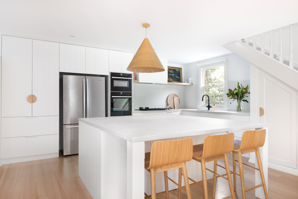 Contemporary l-shaped kitchen in Melbourne with an undermount sink, flat-panel cabinets, white cabinets, stainless steel appliances, light hardwood floors, with island, beige floor and white benchtop.