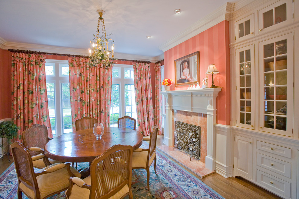 This is an example of a traditional dining room in New York with pink walls, medium hardwood floors and a standard fireplace.