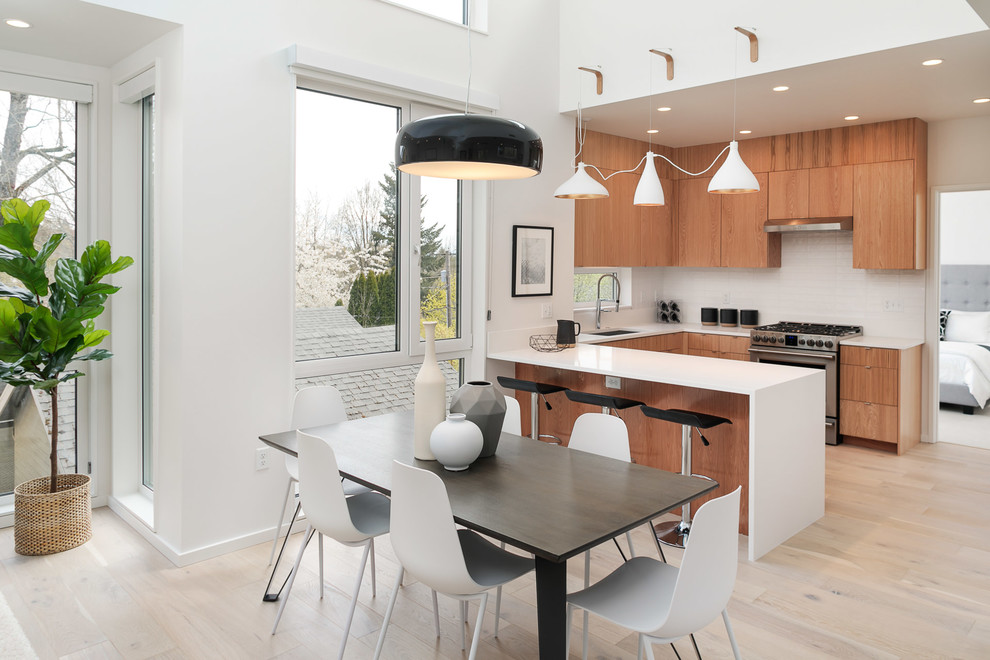 Photo of a contemporary u-shaped eat-in kitchen in Portland with an undermount sink, flat-panel cabinets, medium wood cabinets, white splashback, stainless steel appliances, light hardwood floors, a peninsula, beige floor and white benchtop.