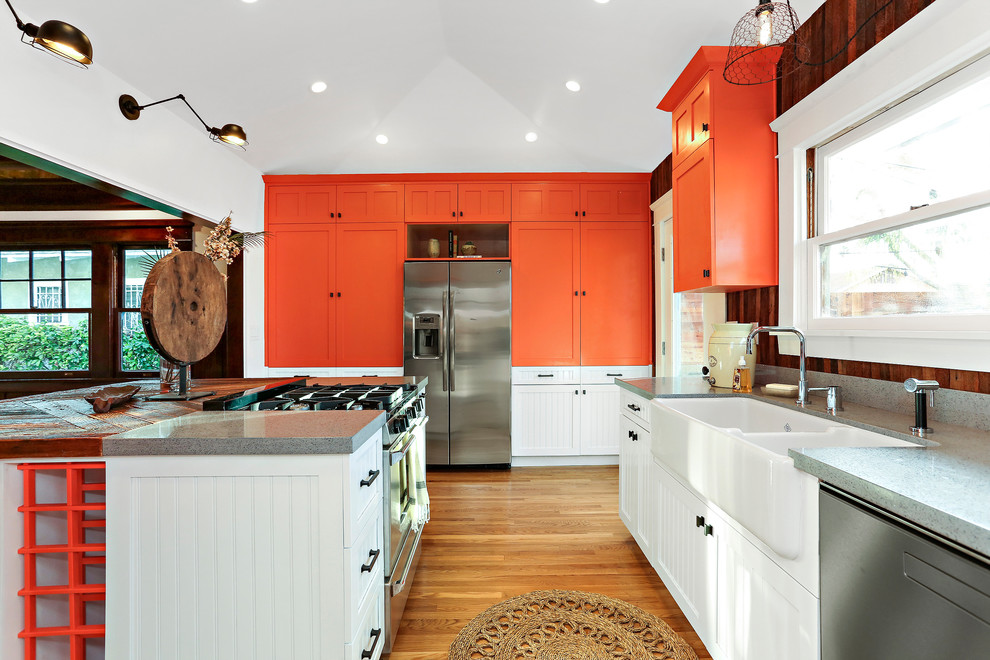 Photo of an arts and crafts u-shaped eat-in kitchen in Los Angeles with a farmhouse sink, shaker cabinets, orange cabinets, brown splashback, timber splashback, stainless steel appliances, medium hardwood floors, with island, brown floor and grey benchtop.