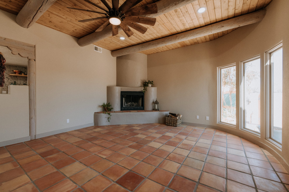 アルバカーキにある高級な広いサンタフェスタイルのおしゃれなLDK (ベージュの壁、テラコッタタイルの床、コーナー設置型暖炉、漆喰の暖炉まわり、オレンジの床) の写真