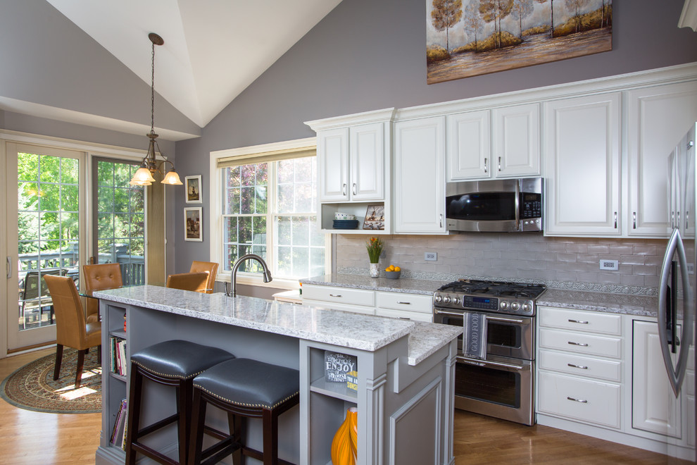 Example of a transitional u-shaped light wood floor eat-in kitchen design in Chicago with a drop-in sink, raised-panel cabinets, white cabinets, granite countertops, gray backsplash, ceramic backsplash, stainless steel appliances and an island