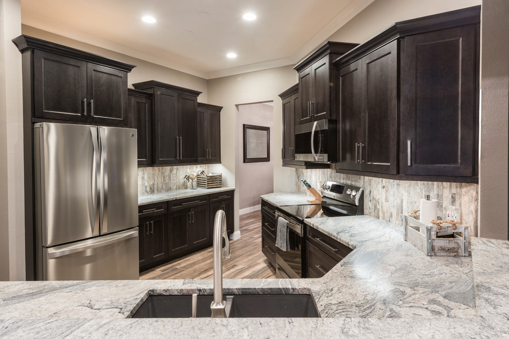 Large transitional l-shaped porcelain tile and brown floor eat-in kitchen photo in Orlando with shaker cabinets, gray cabinets, granite countertops, multicolored backsplash, travertine backsplash, stainless steel appliances, a peninsula and multicolored countertops