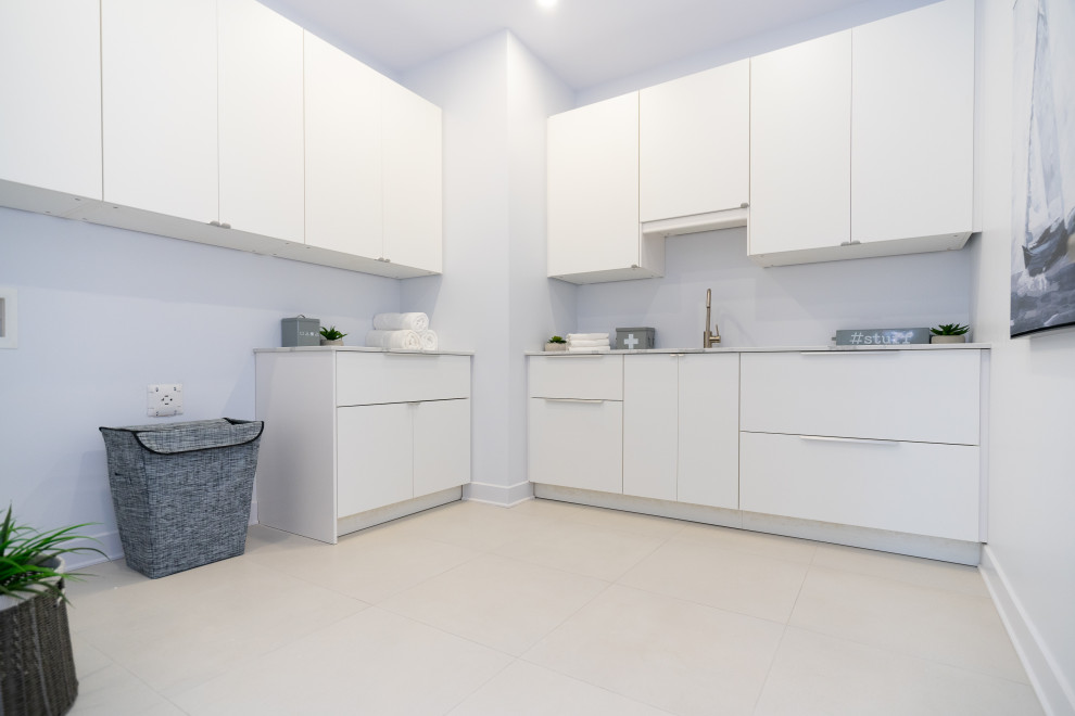Inspiration for a large contemporary l-shaped utility room in Montreal with an undermount sink, flat-panel cabinets, white cabinets, quartz benchtops, grey walls, porcelain floors, a side-by-side washer and dryer, beige floor and white benchtop.