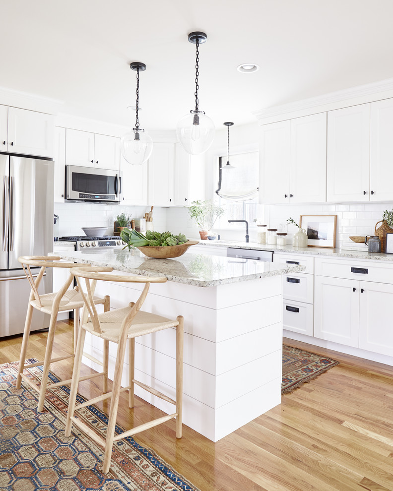 Small country l-shaped kitchen in Bridgeport with a farmhouse sink, shaker cabinets, white cabinets, quartz benchtops, white splashback, subway tile splashback, stainless steel appliances, with island, brown floor, grey benchtop and medium hardwood floors.