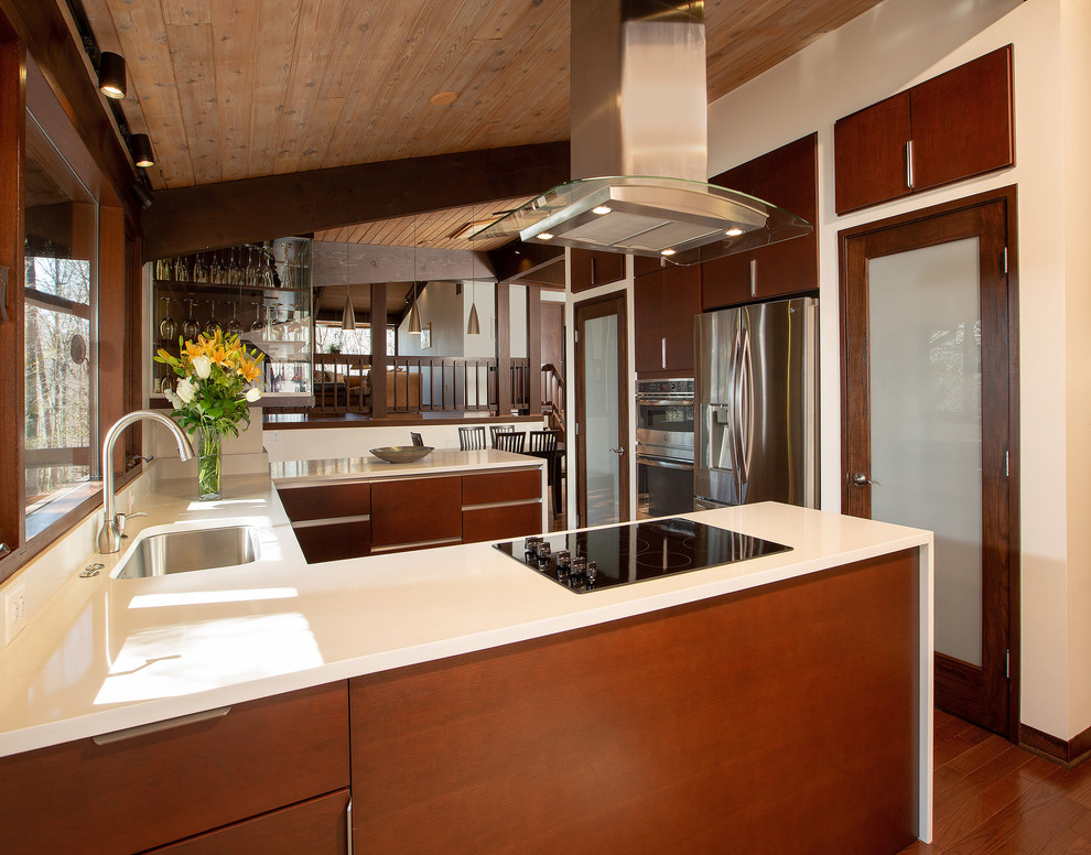 This is an example of a mid-sized midcentury u-shaped eat-in kitchen in DC Metro with a double-bowl sink, flat-panel cabinets, dark wood cabinets, quartzite benchtops, stainless steel appliances, dark hardwood floors, a peninsula, brown floor and white benchtop.