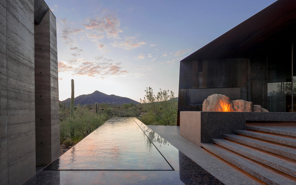 This is an example of a contemporary rectangular infinity pool in Phoenix with a pool house and concrete slab.