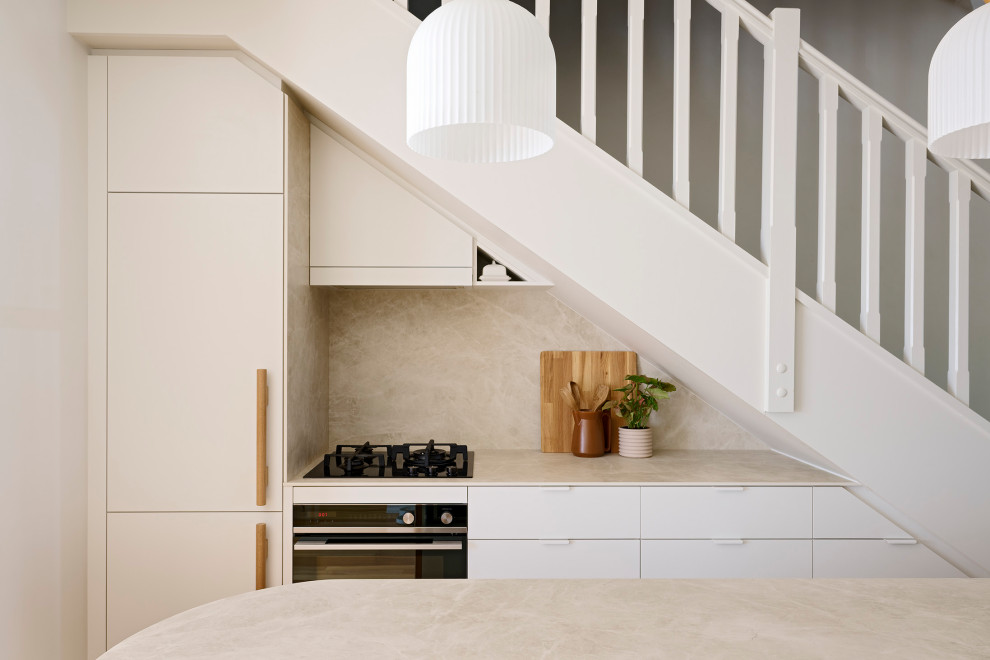 Exempel på ett litet skandinaviskt beige beige kök, med en undermonterad diskho, släta luckor, vita skåp, bänkskiva i kvarts, beige stänkskydd, stänkskydd i porslinskakel, svarta vitvaror, ljust trägolv, en köksö och brunt golv