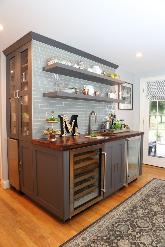 Photo of a mid-sized contemporary single-wall wet bar in Other with an undermount sink, grey cabinets, wood benchtops, grey splashback, glass tile splashback, medium hardwood floors, brown floor, brown benchtop and recessed-panel cabinets.