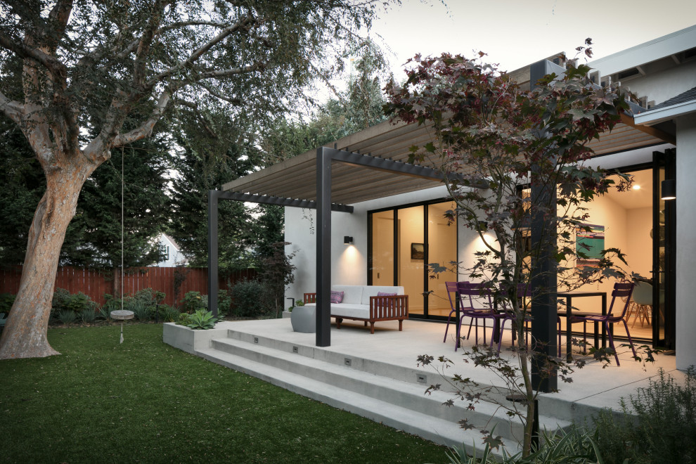 Trendy concrete back porch idea in Los Angeles with a pergola