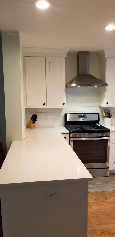 Enclosed kitchen - small transitional galley light wood floor enclosed kitchen idea in Denver with an undermount sink, shaker cabinets, white cabinets, quartz countertops, white backsplash, porcelain backsplash, stainless steel appliances and white countertops