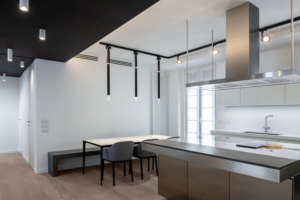 Photo of a large contemporary l-shaped eat-in kitchen in Rome with an undermount sink, flat-panel cabinets, white cabinets, solid surface benchtops, white splashback, light hardwood floors, with island, grey floor and white benchtop.