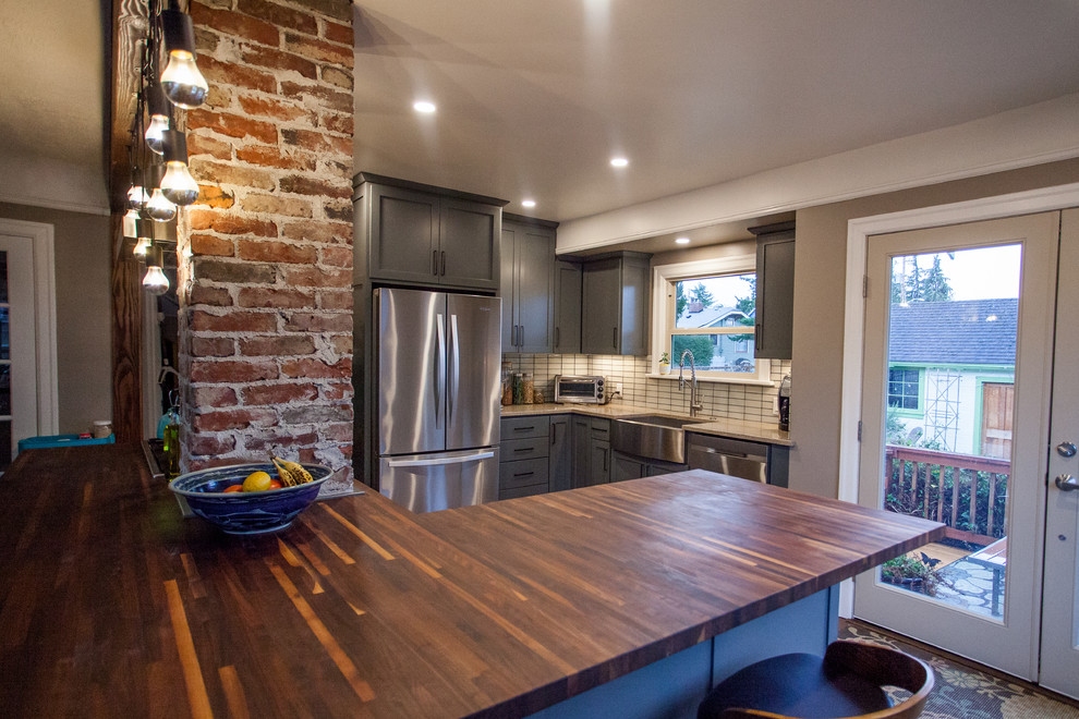 Small transitional l-shaped dark wood floor and brown floor open concept kitchen photo in Seattle with a farmhouse sink, shaker cabinets, gray cabinets, stainless steel appliances, an island, granite countertops, white backsplash, porcelain backsplash and beige countertops