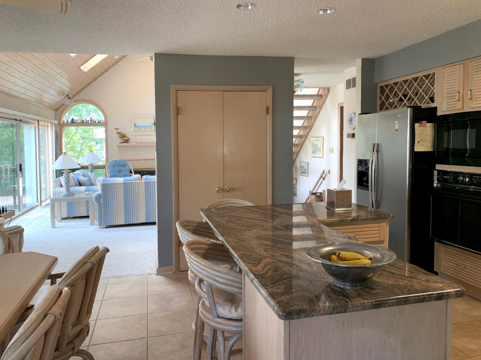 Mid-sized traditional u-shaped eat-in kitchen in DC Metro with louvered cabinets, light wood cabinets, granite benchtops, black appliances, ceramic floors, with island, beige floor and multi-coloured benchtop.