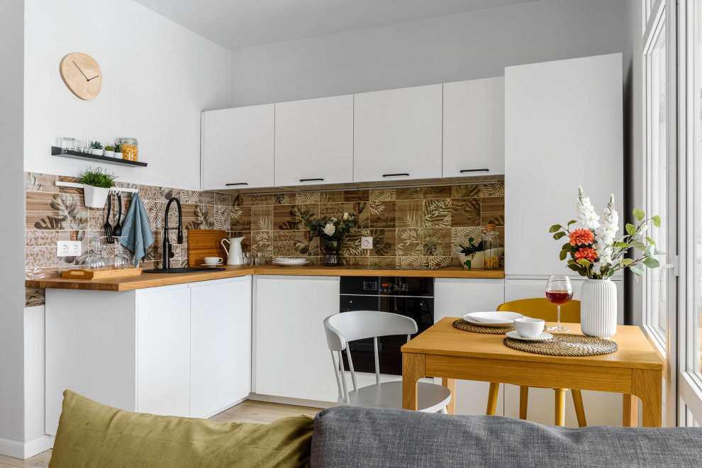 Inspiration for a contemporary l-shaped open plan kitchen in Moscow with a built-in sink, flat-panel cabinets, white cabinets, wood worktops, brown splashback, black appliances, light hardwood flooring, beige floors and brown worktops.