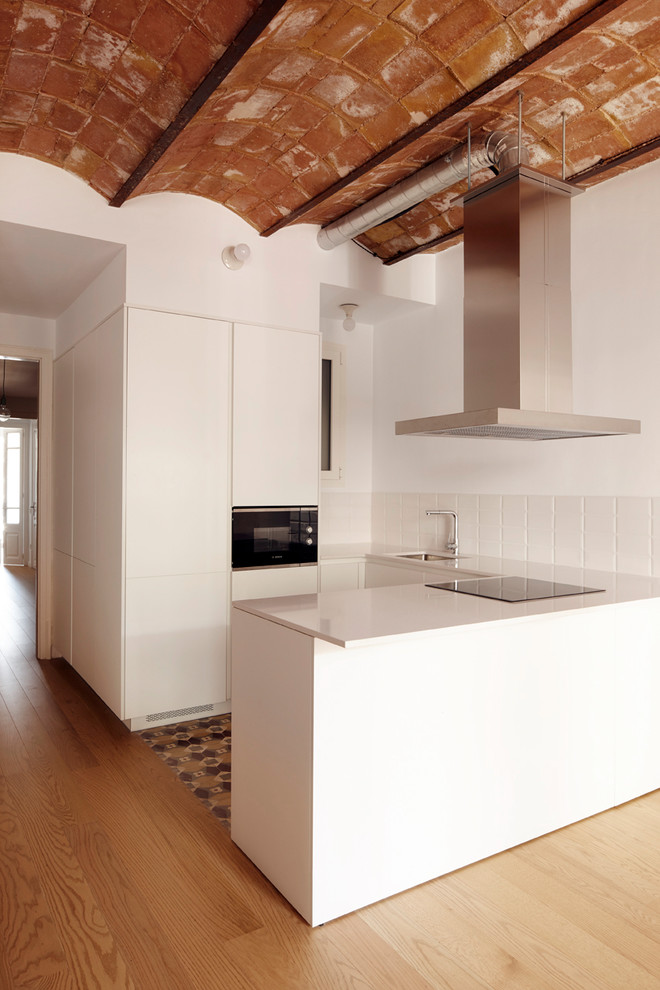 Inspiration for a mid-sized mediterranean u-shaped kitchen in Barcelona with flat-panel cabinets, white cabinets, quartz benchtops, white splashback, ceramic splashback, panelled appliances, ceramic floors, a peninsula, multi-coloured floor, white benchtop and an undermount sink.