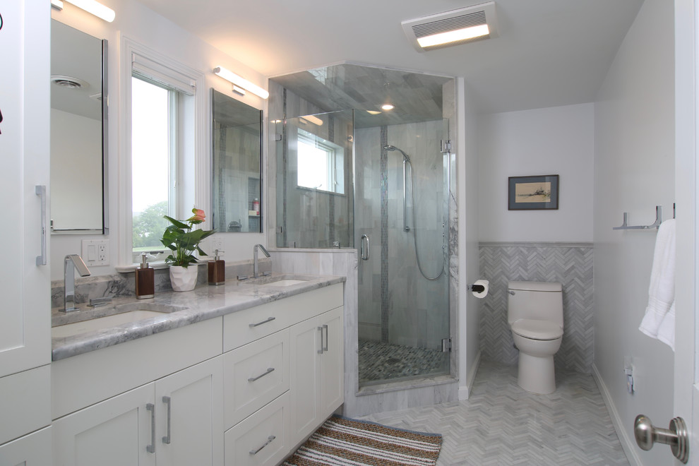 This is an example of a mid-sized transitional master bathroom in Providence with shaker cabinets, white cabinets, a corner shower, a one-piece toilet, gray tile, mosaic tile, white walls, porcelain floors, an undermount sink and marble benchtops.