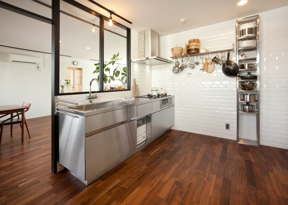 Design ideas for an industrial single-wall separate kitchen in Tokyo Suburbs with a single-bowl sink, flat-panel cabinets, stainless steel cabinets, white splashback, subway tile splashback, dark hardwood floors and brown floor.