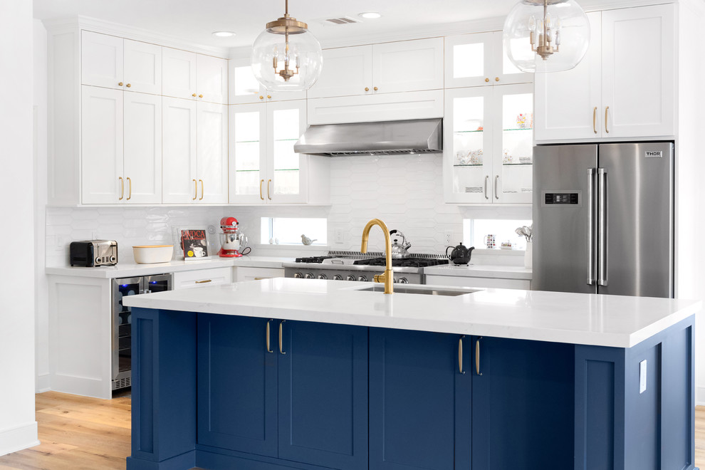 Inspiration for a mid-sized transitional l-shaped eat-in kitchen in Houston with an undermount sink, recessed-panel cabinets, blue cabinets, quartz benchtops, white splashback, subway tile splashback, stainless steel appliances, light hardwood floors, with island, orange floor and white benchtop.