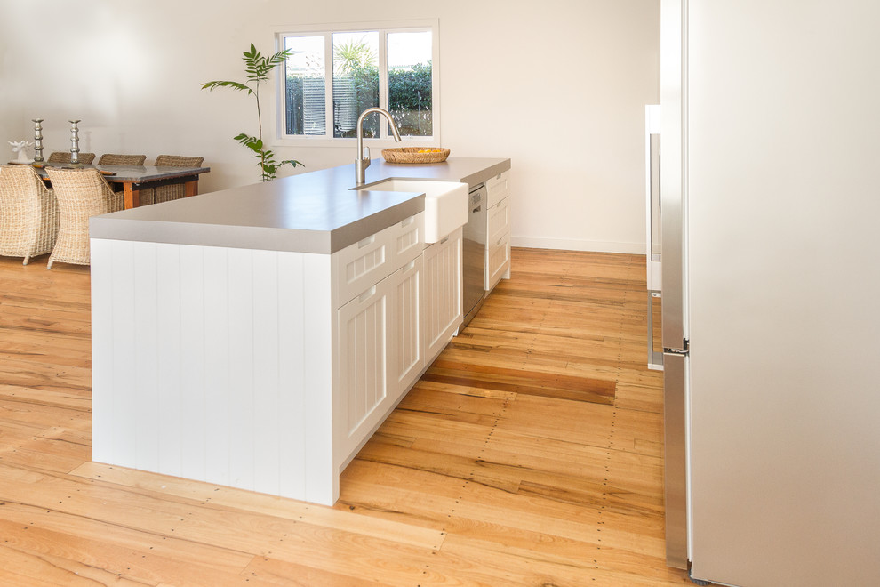Design ideas for a small traditional galley open plan kitchen in Napier-Hastings with a farmhouse sink, recessed-panel cabinets, white cabinets, quartz benchtops, white splashback, ceramic splashback, stainless steel appliances, medium hardwood floors, with island, brown floor and grey benchtop.