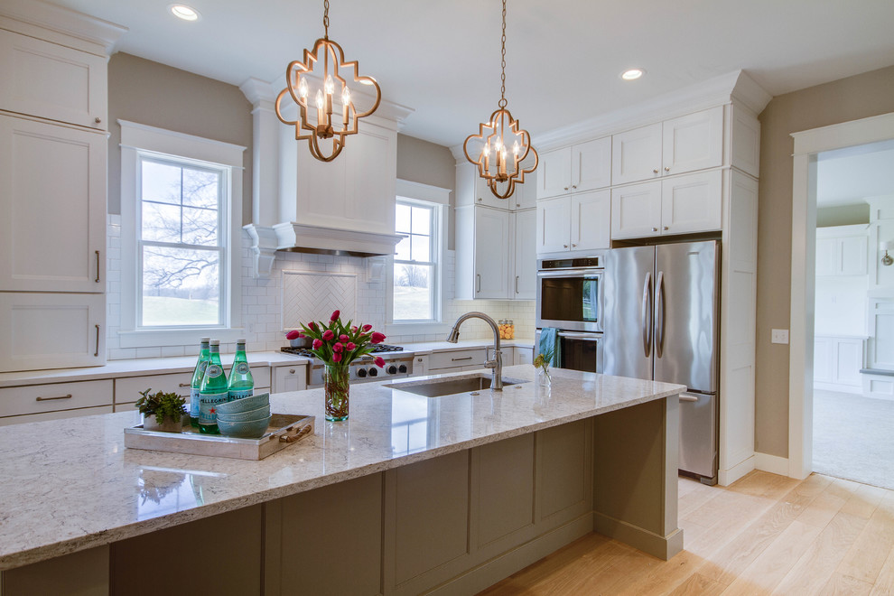 Large transitional l-shaped eat-in kitchen in Grand Rapids with an undermount sink, recessed-panel cabinets, white cabinets, granite benchtops, white splashback, glass tile splashback, stainless steel appliances, light hardwood floors and with island.