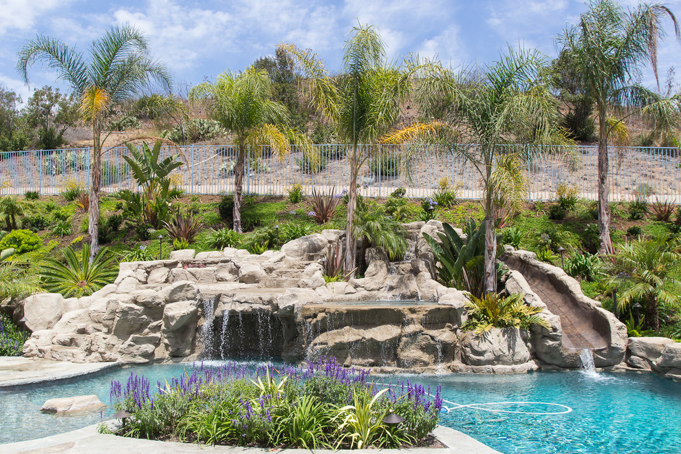 Photo of a large tropical backyard custom-shaped natural pool in Los Angeles with a water slide and natural stone pavers.
