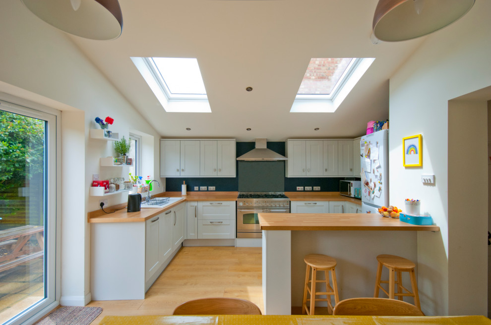 Inspiration for a mid-sized contemporary u-shaped eat-in kitchen in Kent with recessed-panel cabinets, white cabinets, wood benchtops and a peninsula.