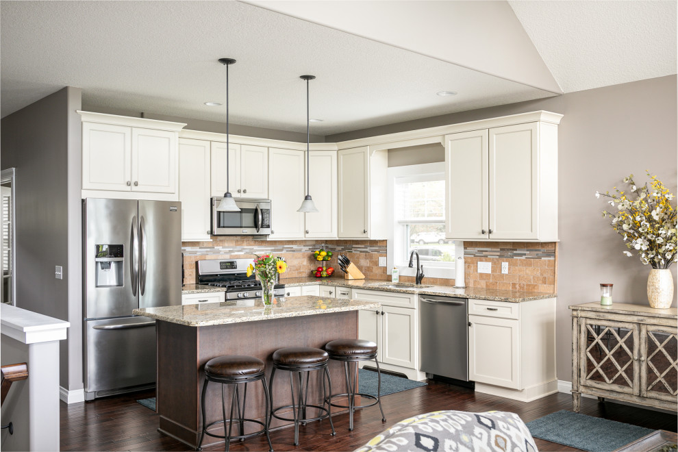 Inspiration for a mid-sized transitional l-shaped medium tone wood floor, brown floor and vaulted ceiling eat-in kitchen remodel with an undermount sink, flat-panel cabinets, white cabinets, granite countertops, beige backsplash, stone tile backsplash, stainless steel appliances, an island and beige countertops